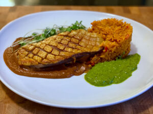 Pan-roasted duck breast with crispy skin, mole poblano, Mexican red rice, and bright green cilantro-lime sauce, inspired by Jake Kelley's Holy Mole dish on MasterChef Season 16.